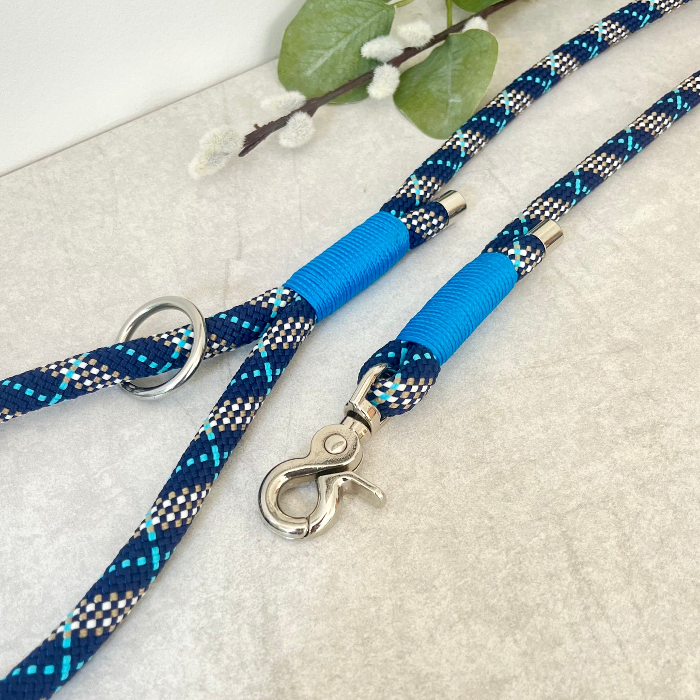 Tartan Blue rope lead with Royal Blue whipping securing a swivel clip at one end and fastening a handle at the other. The handle has an O-ring attached. Each end of the rope is finished with a metal end cap. All hardware for this lead is in Silver