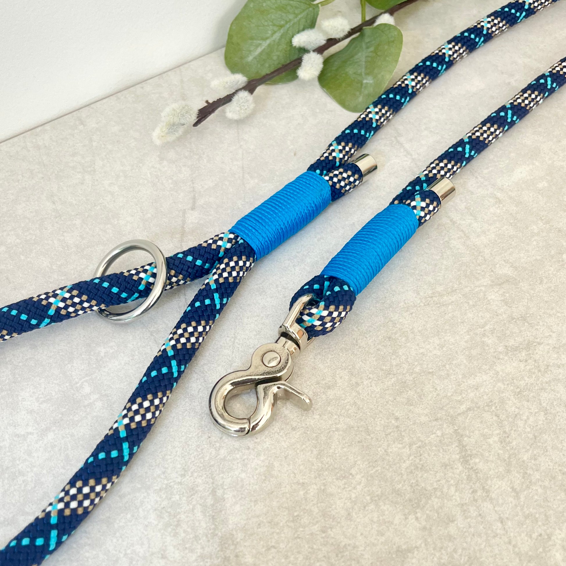 Tartan Blue rope lead with Royal Blue whipping securing a swivel clip at one end and fastening a handle at the other. The handle has an O-ring attached. Each end of the rope is finished with a metal end cap. All hardware for this lead is in Silver