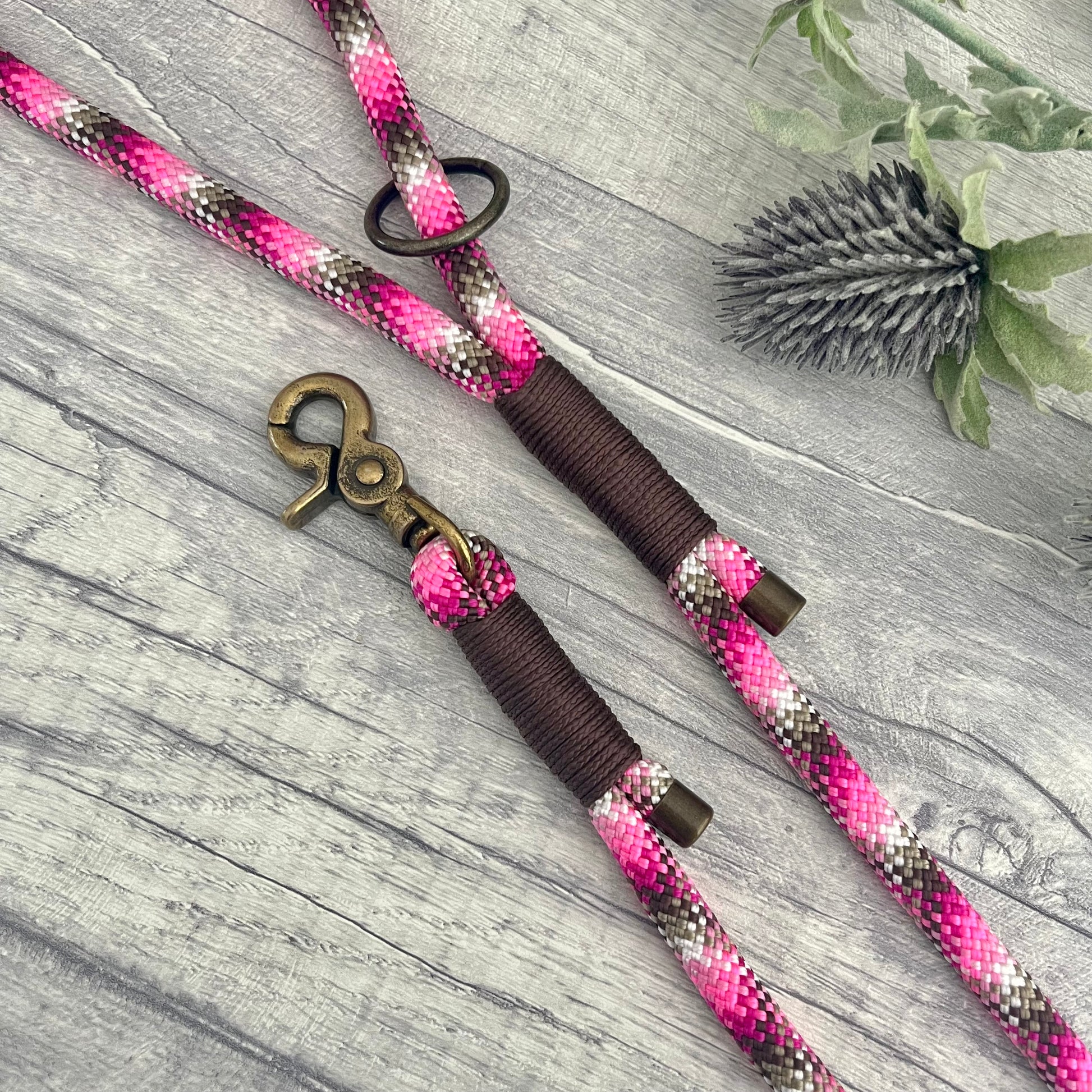 Cowgirl, pink mix Paracord rope lead with Brown whipping securing each end together. At each end of the rope there is a metal end cap, a clip to connect to a collar at one end and a O-ring fixed to the handle. All hardware is Antique Brass